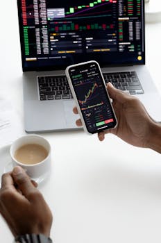 Person analyzing stock market trends on smartphone with laptop background