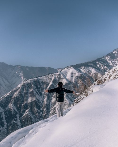 Free A man embraces the majestic views of snow-covered mountains under a clear blue sky. Stock Photo