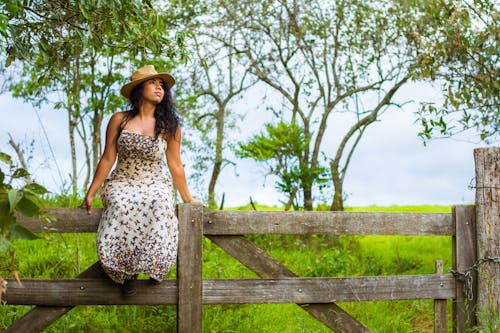 A Woman in Tube Dress Wearing a Hat while Sitting on a Wooden Fence