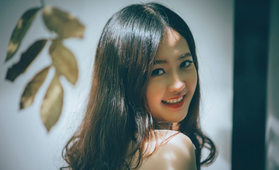 Portrait of a beautiful Asian woman with long hair smiling warmly, captured in an elegant studio setting.