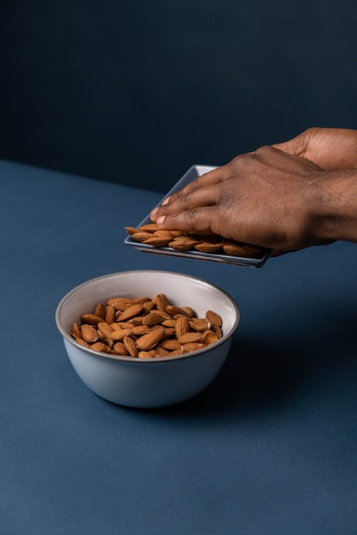 woman pushing almonds from plate into bowl on a table