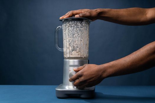 Close-up of male hands operating a blender in a kitchen setting.