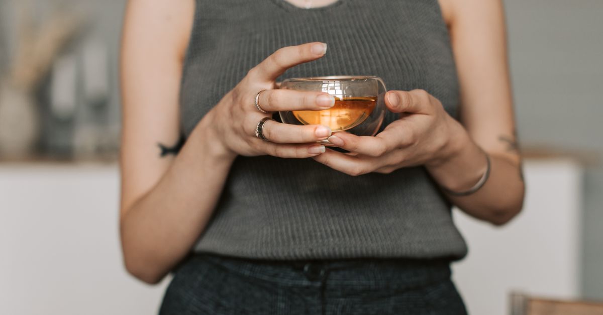 A person in a gray tank top enjoying a warm herbal tea indoors. Perfect serene lifestyle imagery.
