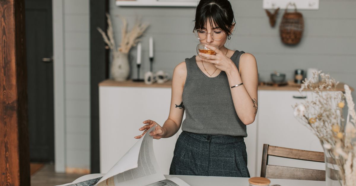 A woman in a comfortable home setting enjoys tea while reading, embodying relaxation and calm.