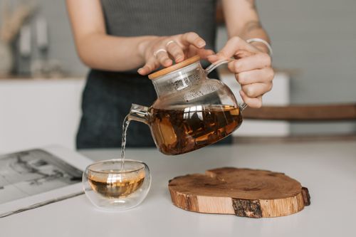 Free Woman pouring hot tea from a glass teapot into a cup, indoors setting. Stock Photo