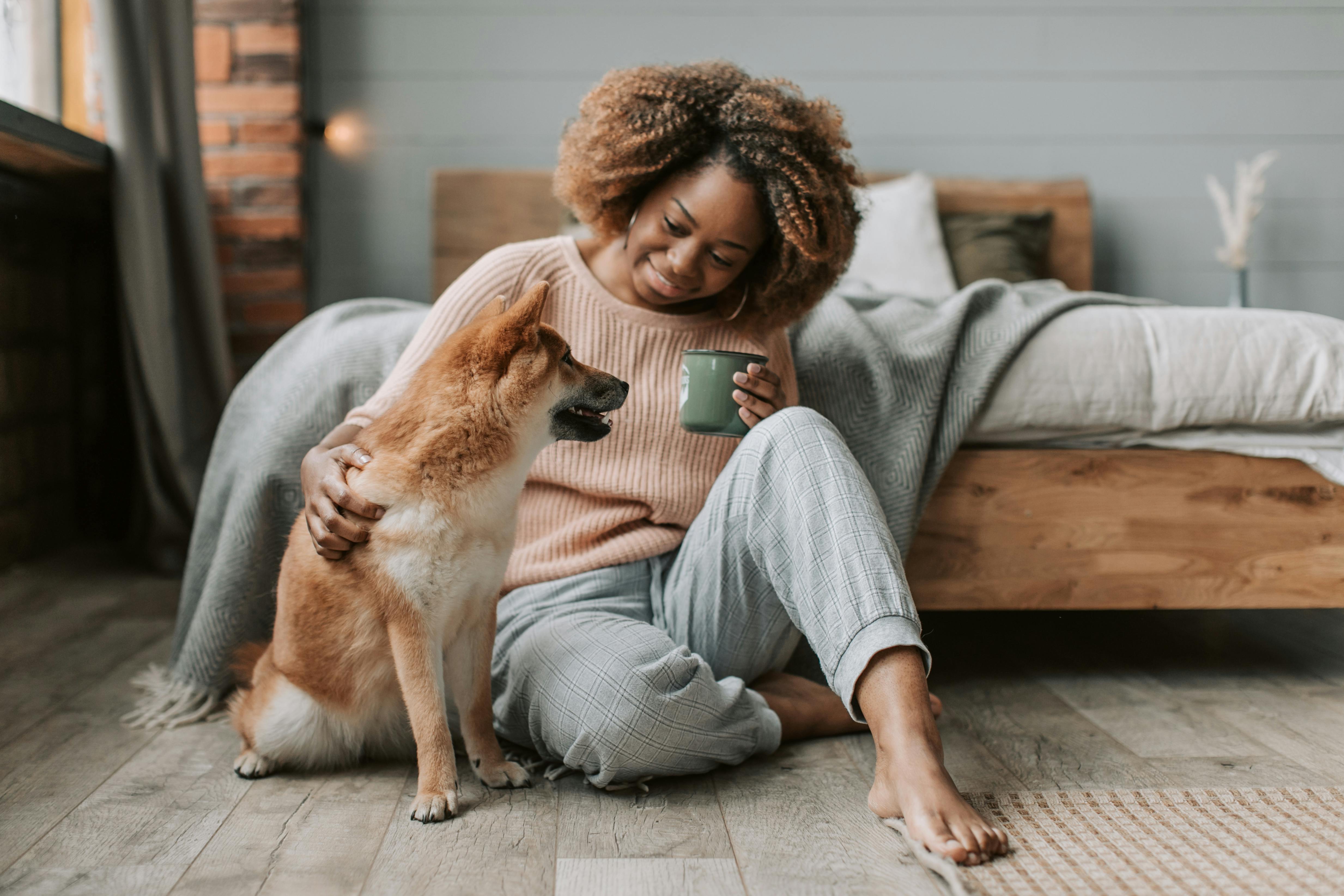 woman sitting on wooden floor drinking coffee with her dog