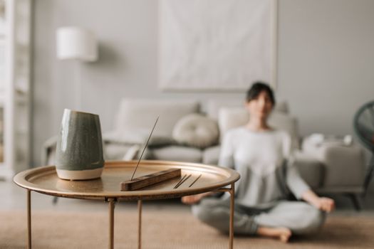 Calm living room scene with incense and a woman meditating, perfect for relaxation concepts.