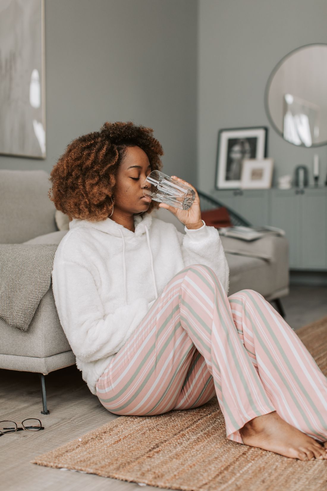 Perempuan bersantai di sofa rumah sambil minum segelas air