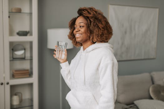 African American woman in a cozy hoodie with a glass of water, starting her day indoors.