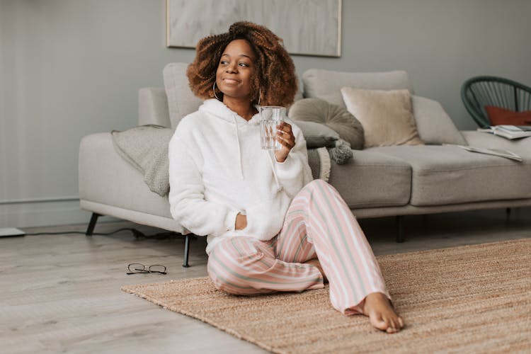 A Woman Sitting On The Floor Holding A Glass Of Water 