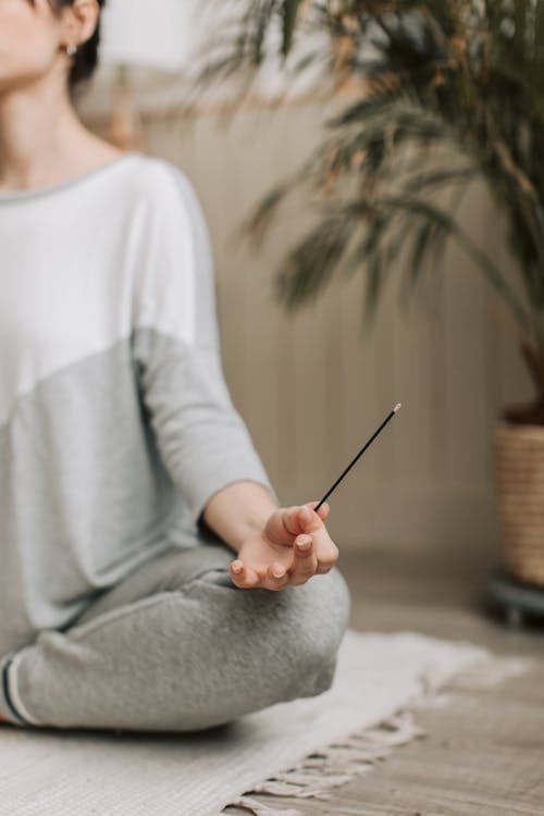 Woman in White and Gray Long Sleeve Shirt Holding a Incense Stick