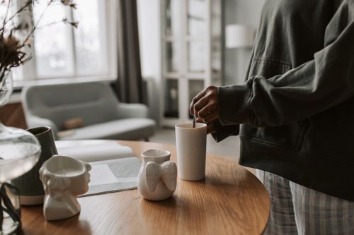 Free A person wearing a hoodie enjoys a warm drink in a modern, comfortable living room setting. Stock Photo