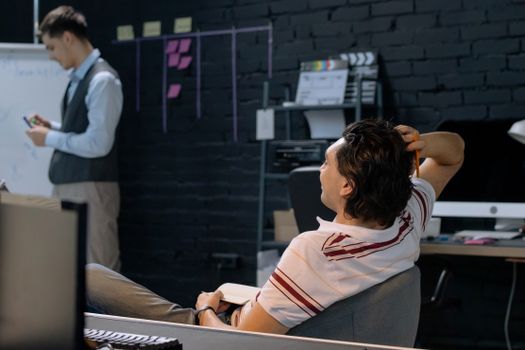 Two men engaged in a casual office meeting, one using a whiteboard, reflecting modern business dynamics.