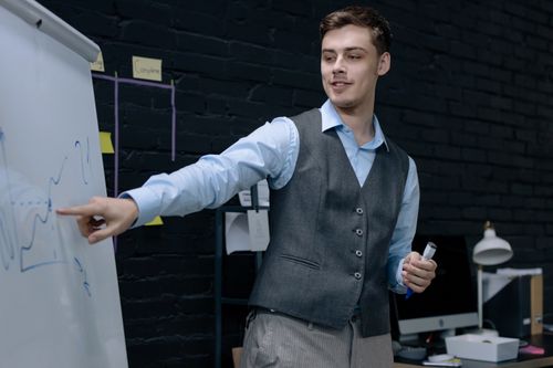 Free Businessman presenting data on a whiteboard in a contemporary office setting. Stock Photo
