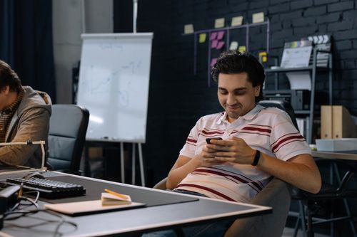 Free A young man using a smartphone in a modern office environment with conference room features. Stock Photo