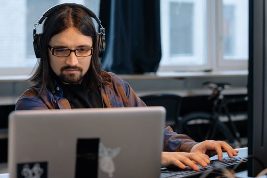 Office worker wearing headphones while concentrating on laptop tasks.