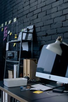 A sleek, contemporary office setup with computer and office supplies against a black brick wall.