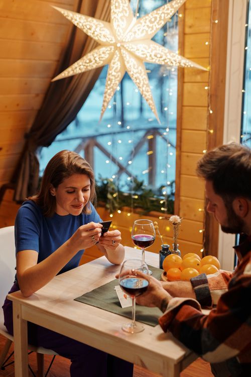 Free A couple enjoys a cozy evening indoors with wine and holiday decor under warm lighting. Stock Photo