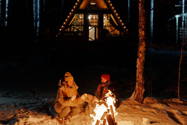 Couple Sitting By Bonfire At Night In Winter