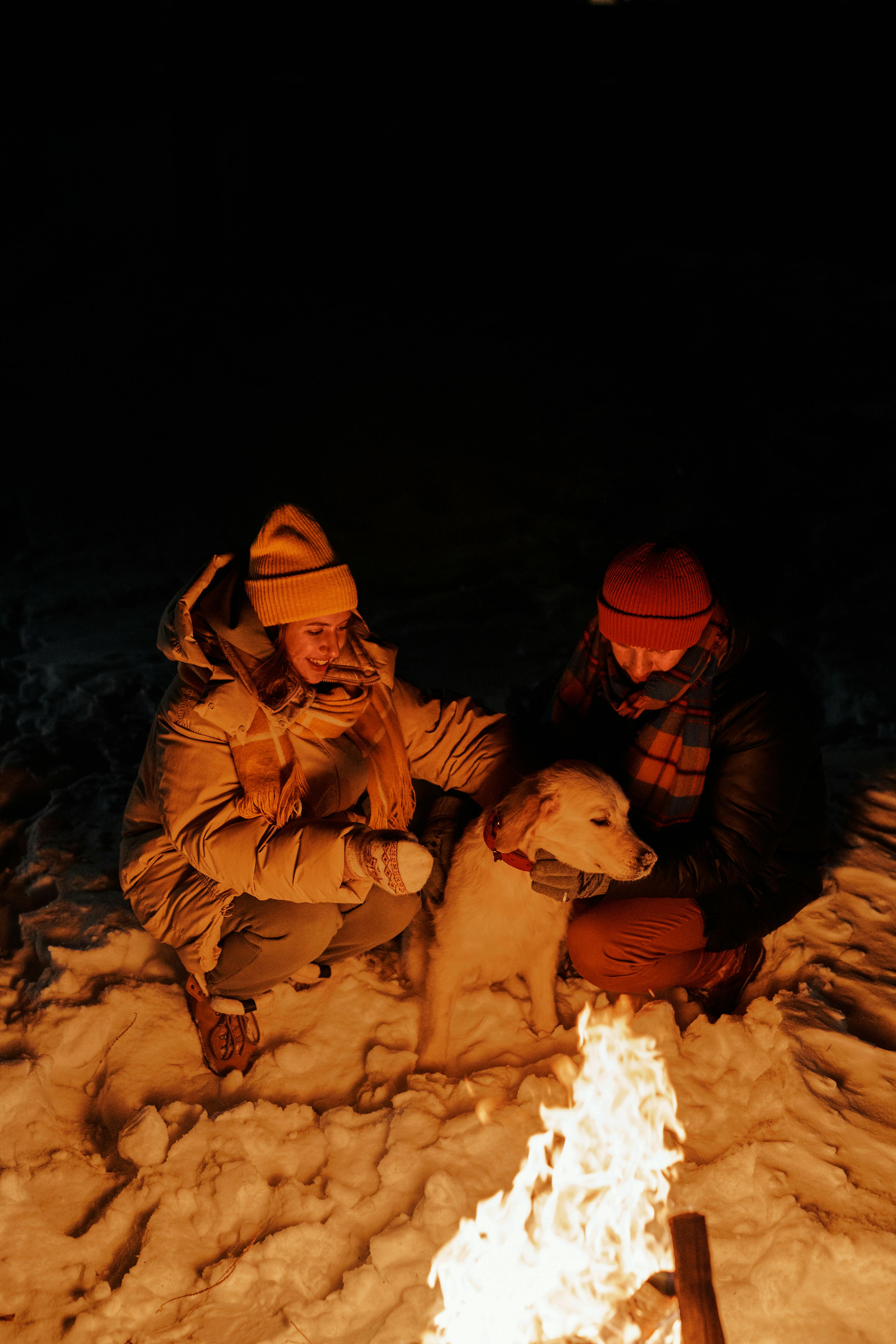 couple and their dog sitting next to a bonfire in winter