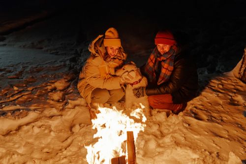 Free A couple enjoying a warm campfire with their dog on a snowy winter night, creating a cozy and intimate atmosphere. Stock Photo