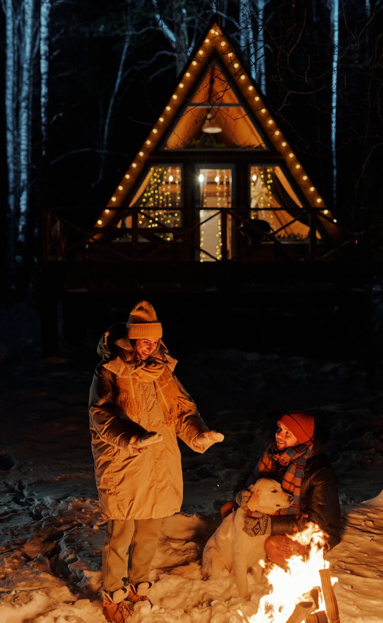 Smiling Couple With Dog By Bonfire At Night