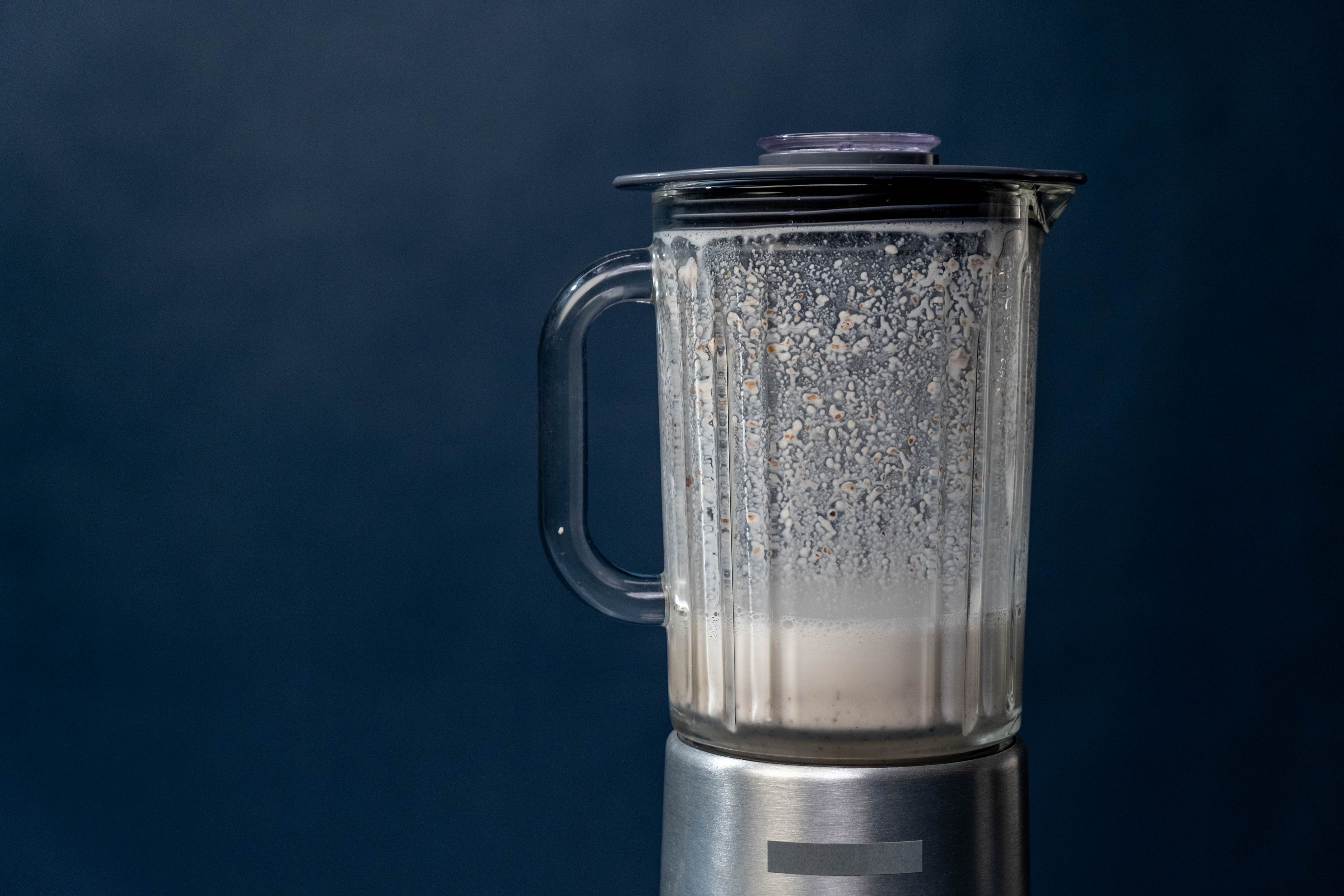 Close-up of a silver blender making a milkshake against a blue background, studio shot.
