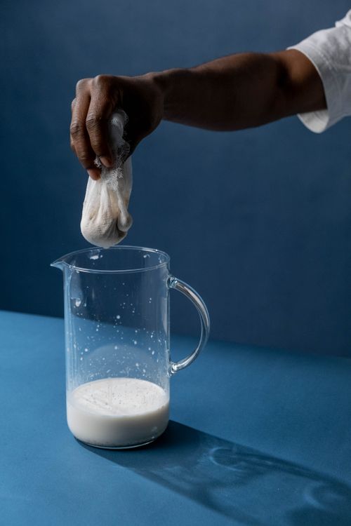 Free A hand squeezes liquid through cloth into a glass jug against a blue background. Stock Photo