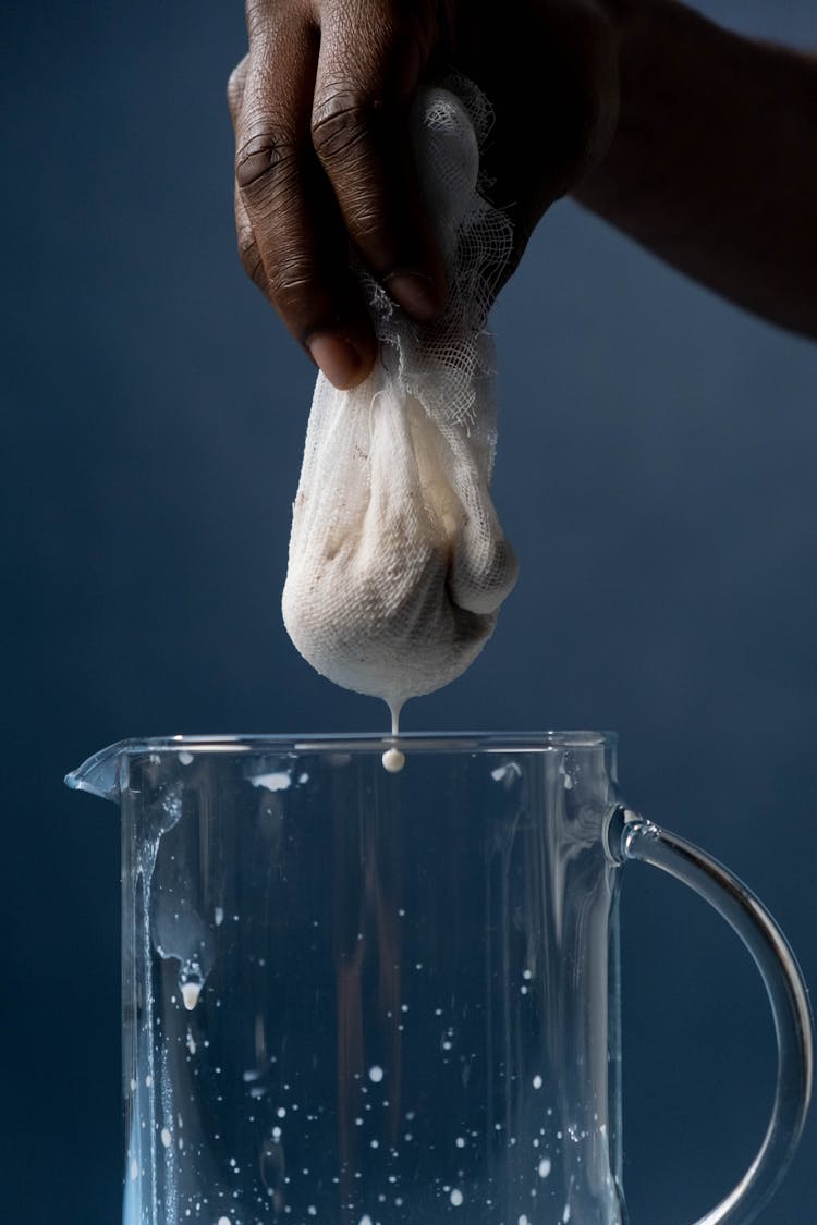 A Person Holding A Cheesecloth With Dripping Milk