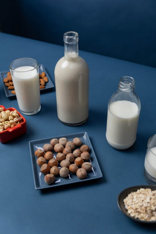 Fresh Milk on Glass Containers Beside Plates of  Nuts 