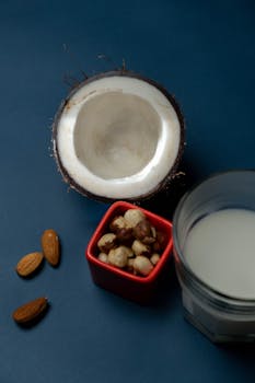 A vertical shot of almonds, macadamia nuts, coconut, and plant-based milk on a dark background.