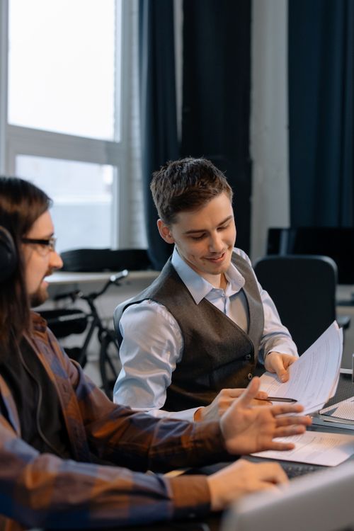 Free Two young men collaborating with documents in a modern office setting, emphasizing teamwork and productivity. Stock Photo