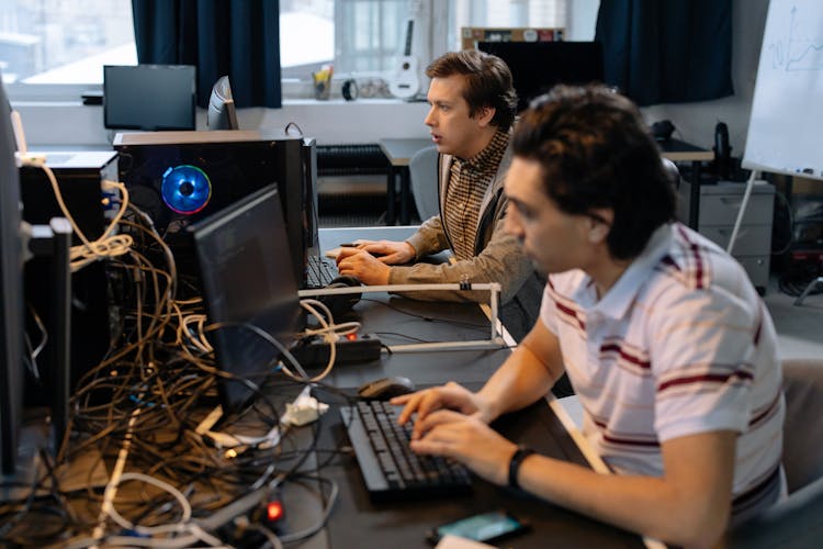 Men Sitting At The Desks In An Office And Using Computers 