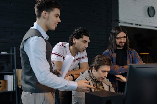 Free Employees Discussing Project Standing Over Programmer Working at a Computer Stock Photo