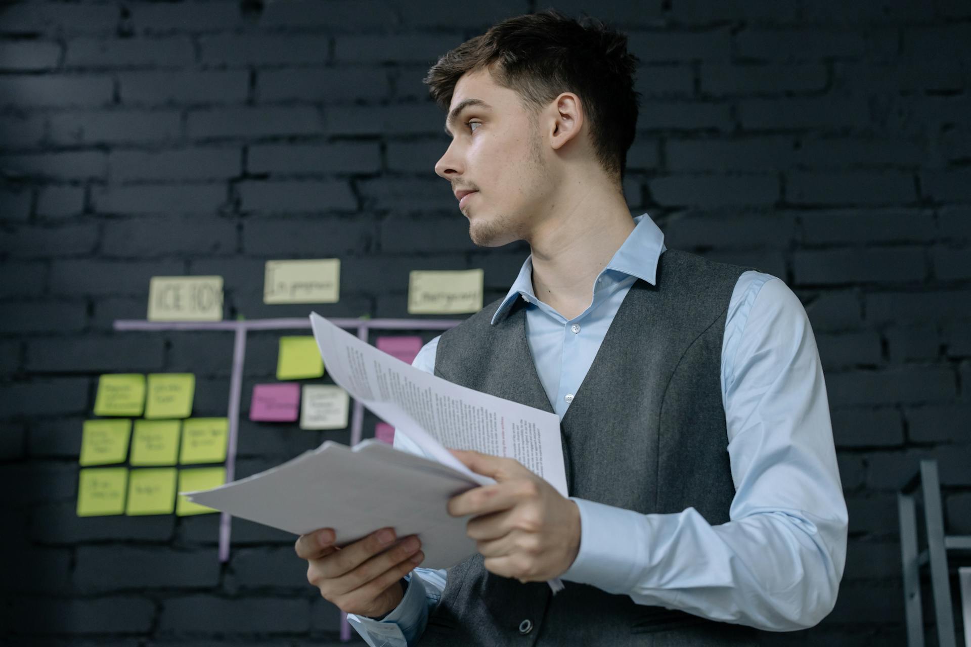 Young male professional analyzing project documents in a modern office setting with a task board.