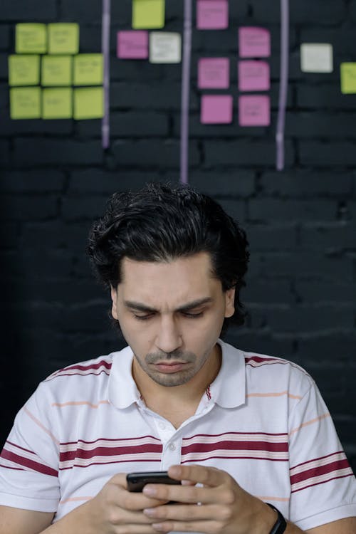 Man Wearing a Striped Shirt Browsing a Smartphone