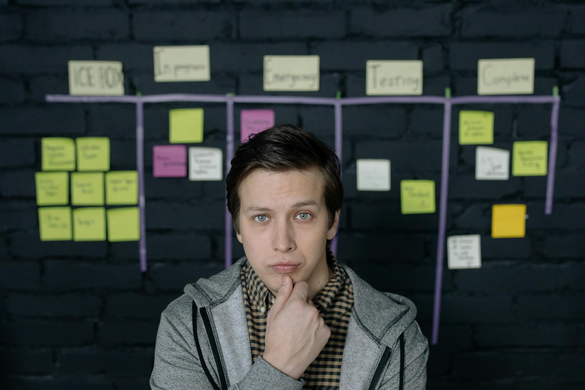 Pensive man in a startup workspace pondering tasks on a project board.