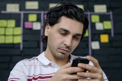 Free Focused man using smartphone indoors with sticky notes on wall. Stock Photo