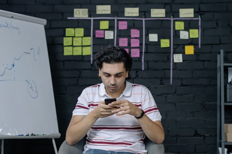 Man In Stripe Polo Shirt Sitting On Chair Using Smartphone