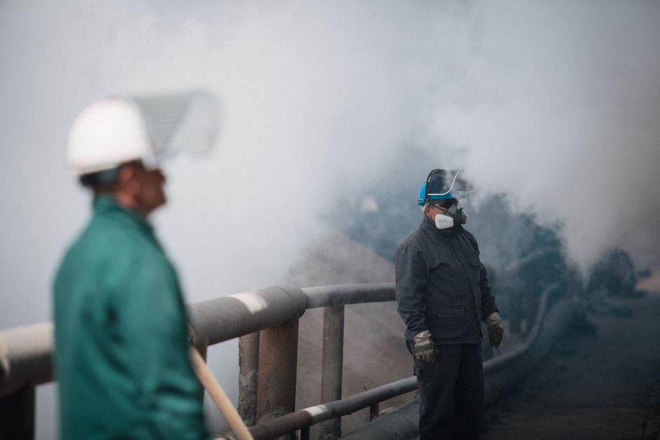 Trabajadores industriales con equipo de seguridad en medio de humo denso, ilustrando la contaminación y las medidas de seguridad.