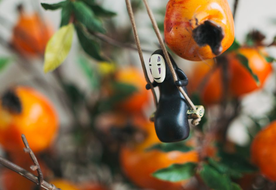 A charming figurine swings among ripe persimmons, creating a playful scene.