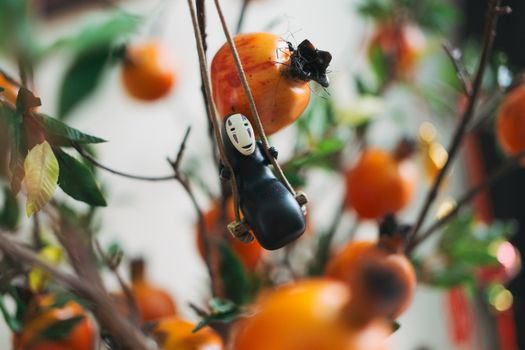 A whimsical toy figure hangs from branches among ripe orange persimmons in a playful setting.
