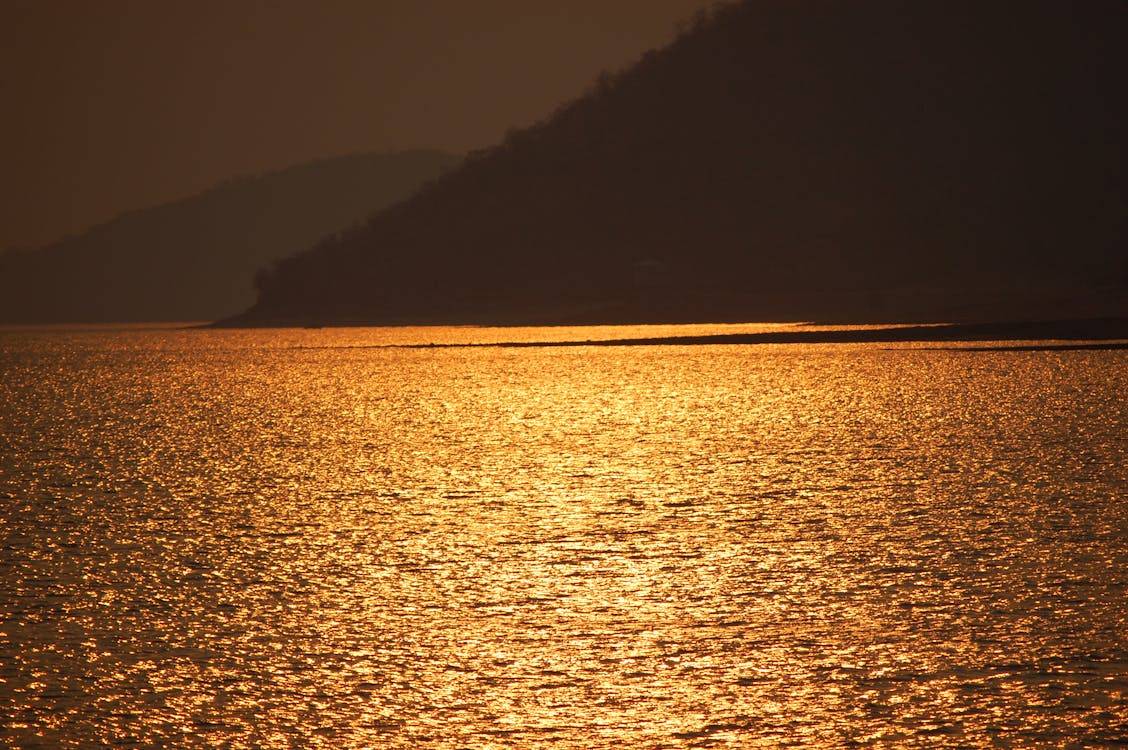 бесплатная Синее море возле коричневой горы во время заката Стоковое фото