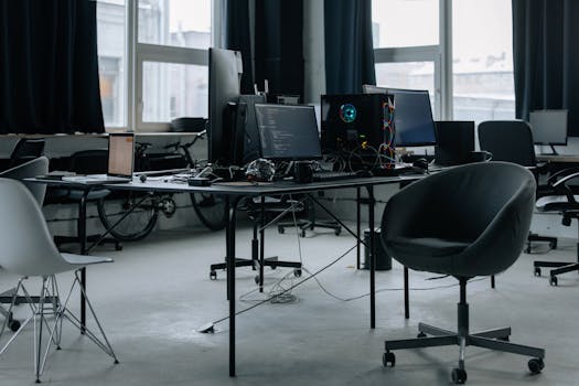 Discover a modern office workspace with computers, chairs, and natural light from large windows.