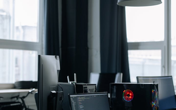 A modern office desk with computers, monitors, and tech equipment in a bright room.