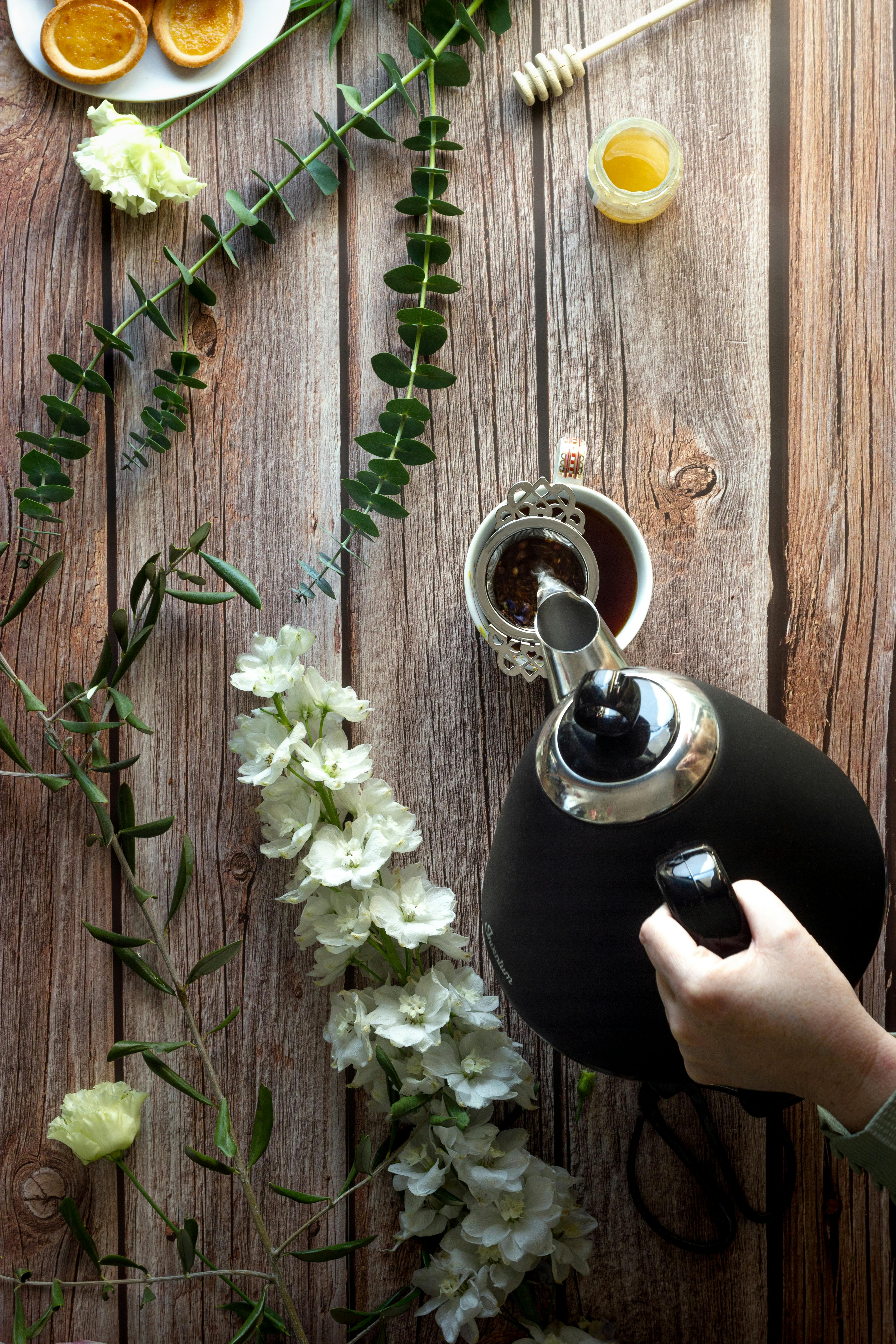 An overhead shot of a hand pouring tea into a cup with floral decoration on wooden surface.