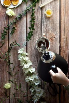 An overhead shot of a hand pouring tea into a cup with floral decoration on wooden surface.