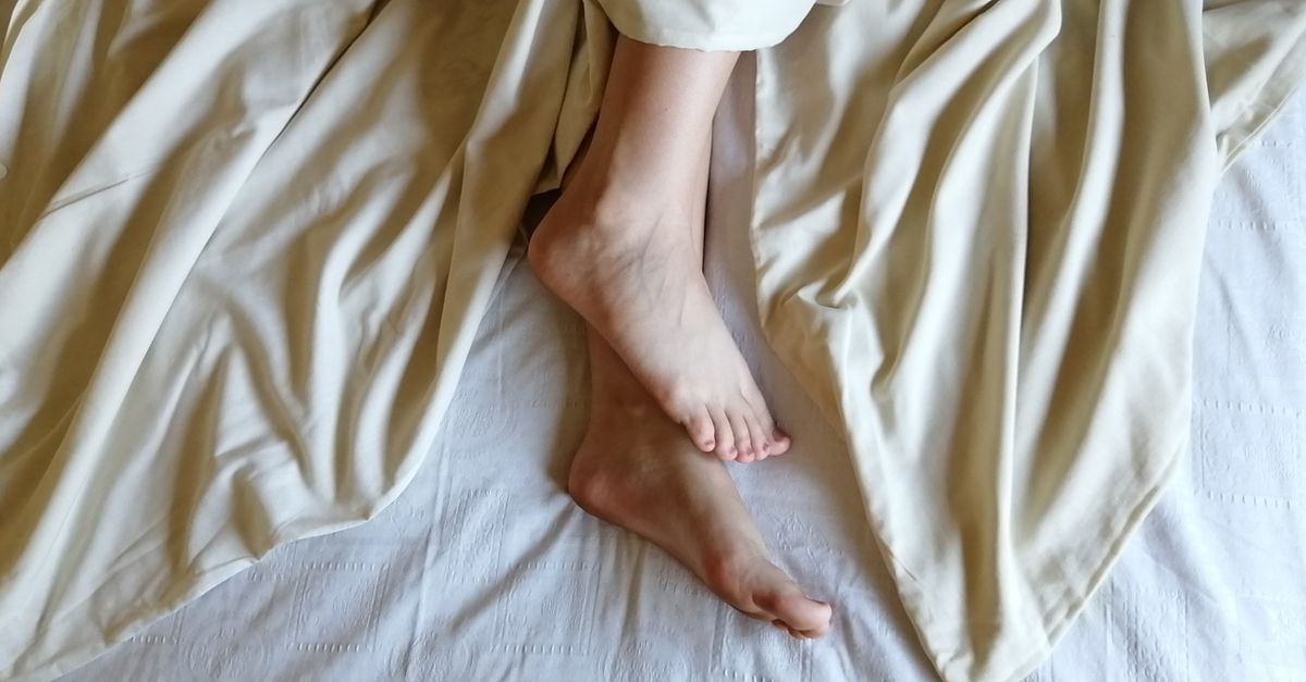 Um par de pés aparece debaixo de lençóis de linho cor creme em um ambiente aconchegante e relaxado.
