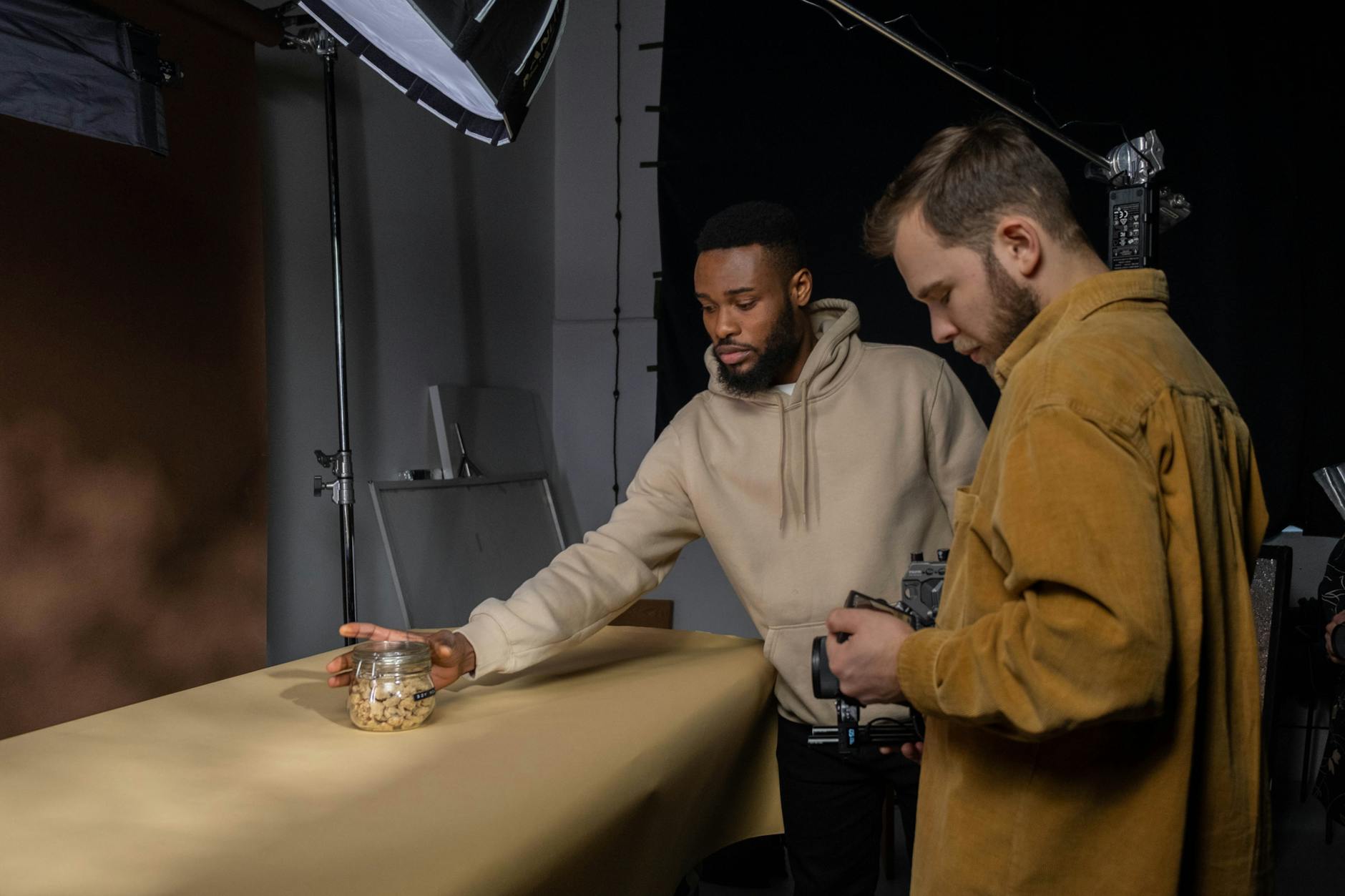 Two men collaborate in a studio setting, preparing for a product photoshoot with professional equipment.