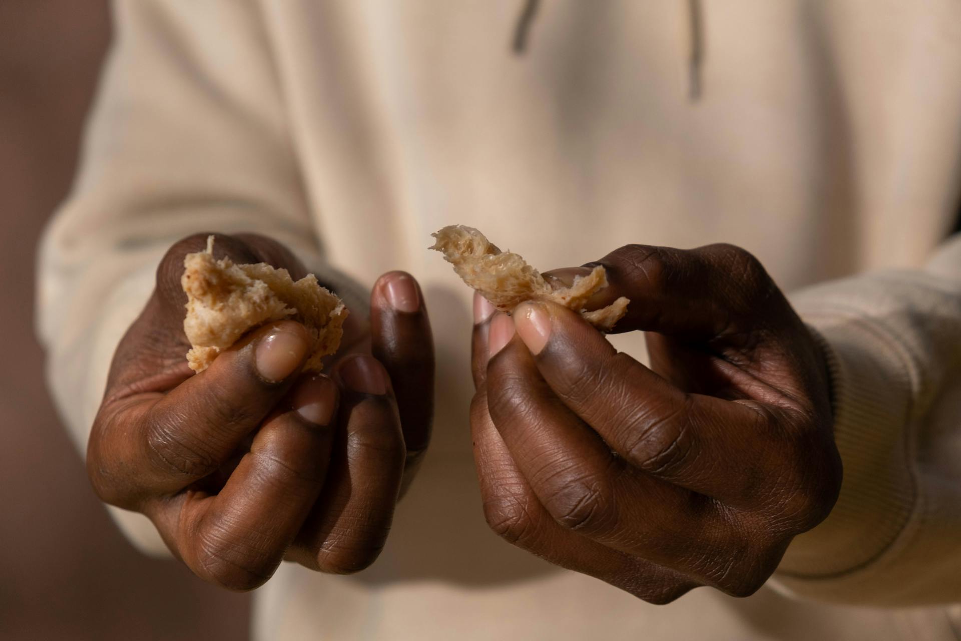 Close-up of adult hands breaking a piece of bread, highlighting texture and detail.